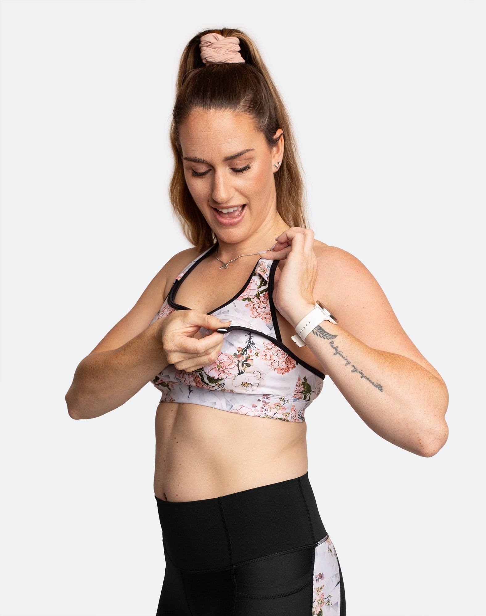 Breastfeeding mum showing the nursing function of maternity sports bra with white floral print and black trim