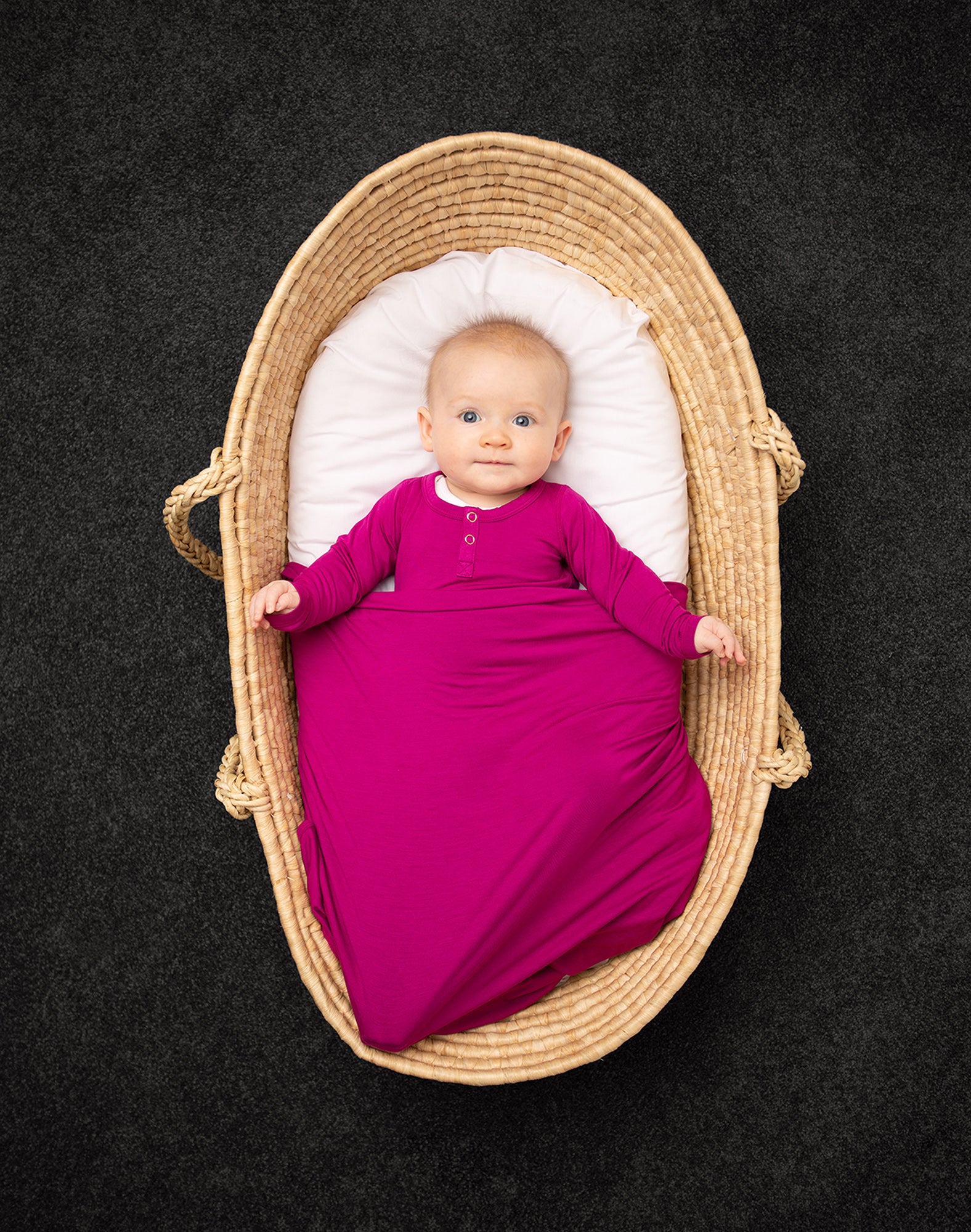 4 month old baby in matching bright pink onsie and swaddle in moses basket